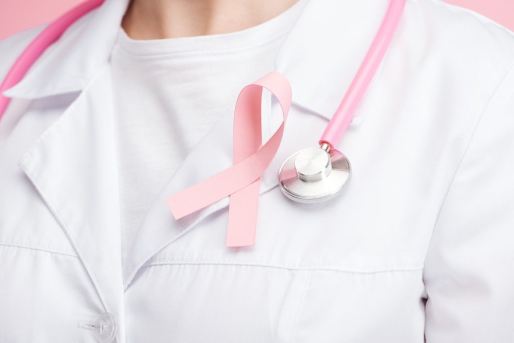close up view of doctor in white coat with pink breast cancer sign